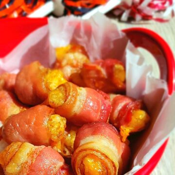 bacon wrapped tater tots in red bowl with pom poms on a stick in background