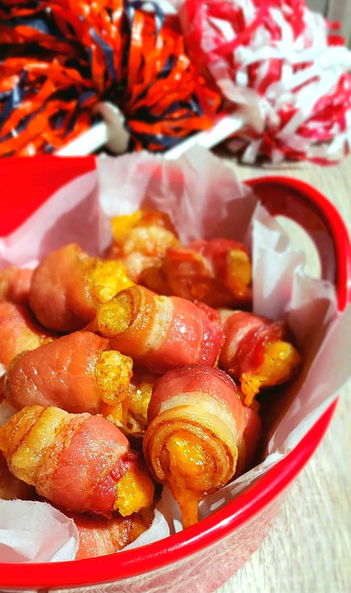 bacon wrapped tater tots in red bowl with pom poms on a stick in background