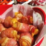 Bacon Wrapped Cheesy Tator Tots in red bowl with cheer pom poms in background for the big game