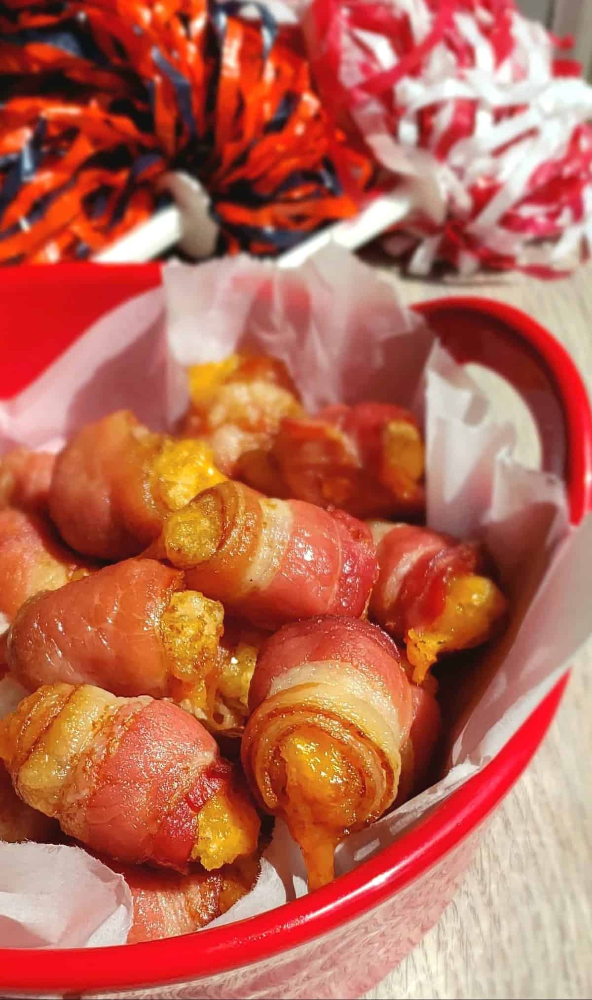 Bacon Wrapped Cheesy Tator Tots in red bowl with cheer pom poms in background for the big game