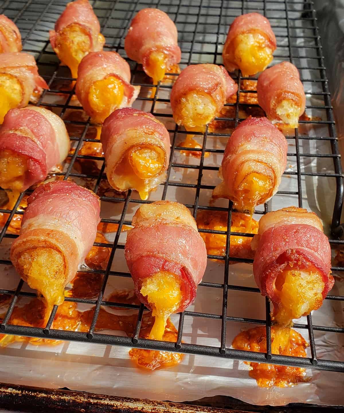 Baked bacon wrapped tater tots on wire rack with cheese oozing out