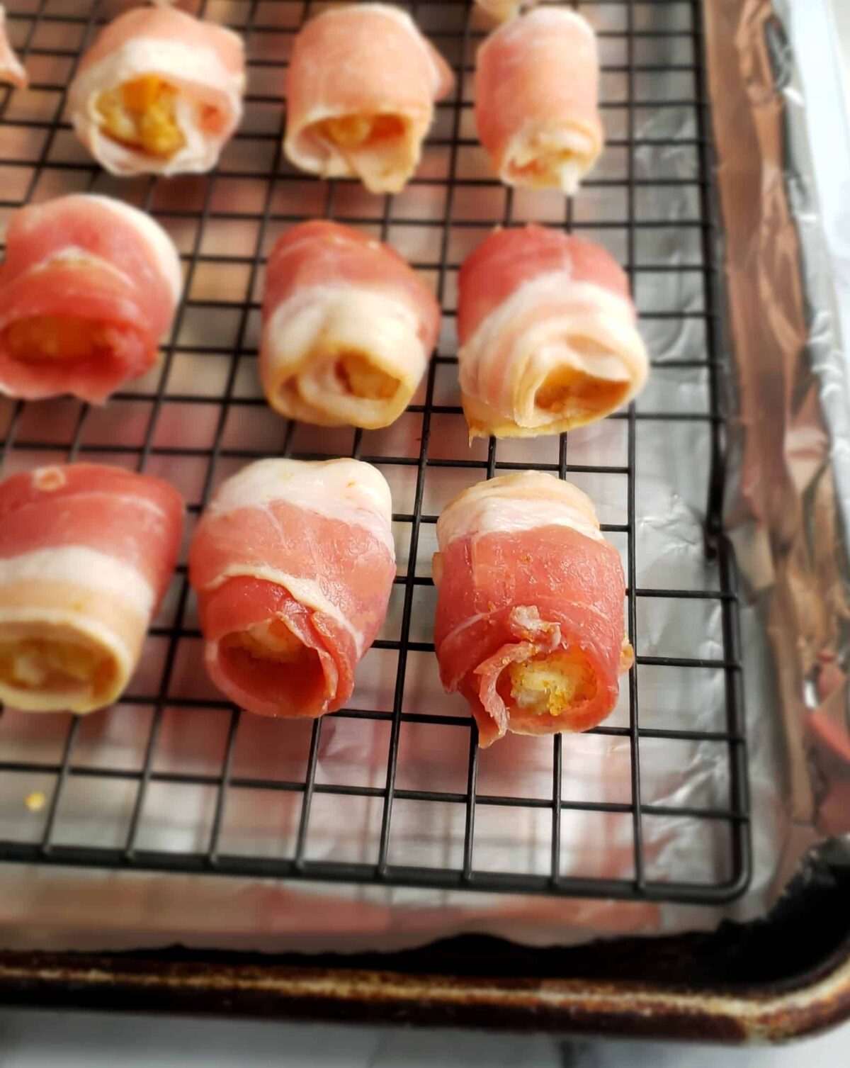 Close up raw bacon wrapped tator tots on wire rack
