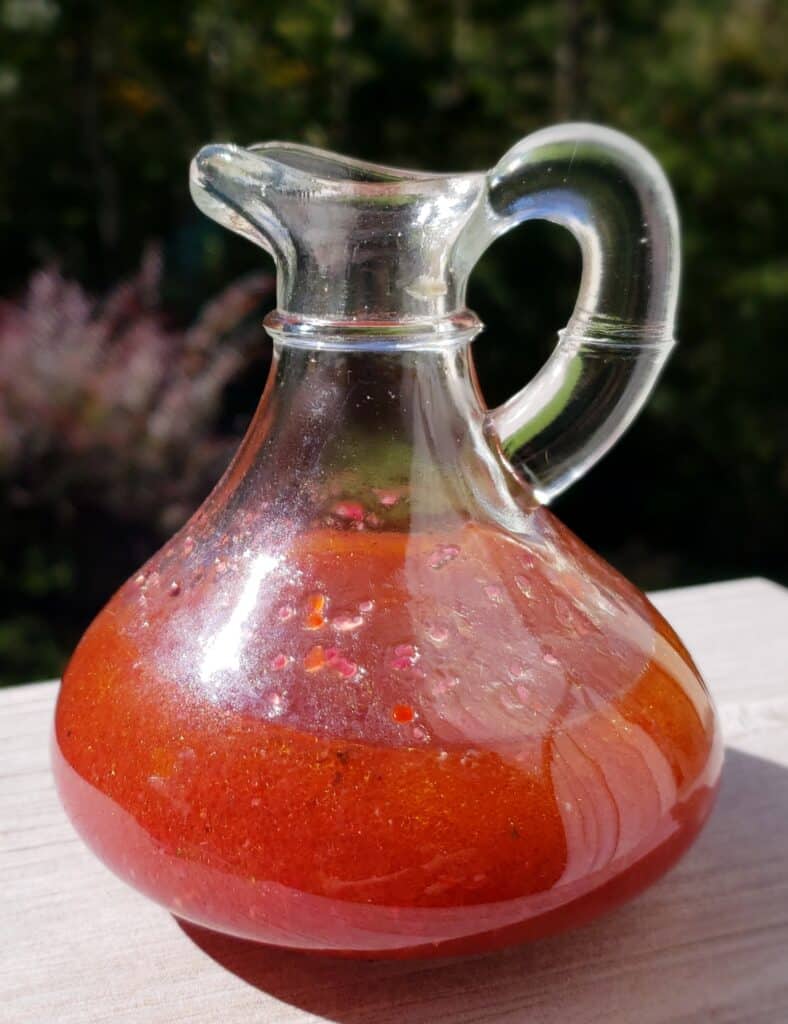 Glass salad dressing bottle full of blackberry vinaigrette made with homemade blackberry vinegar substituting for black raspberries