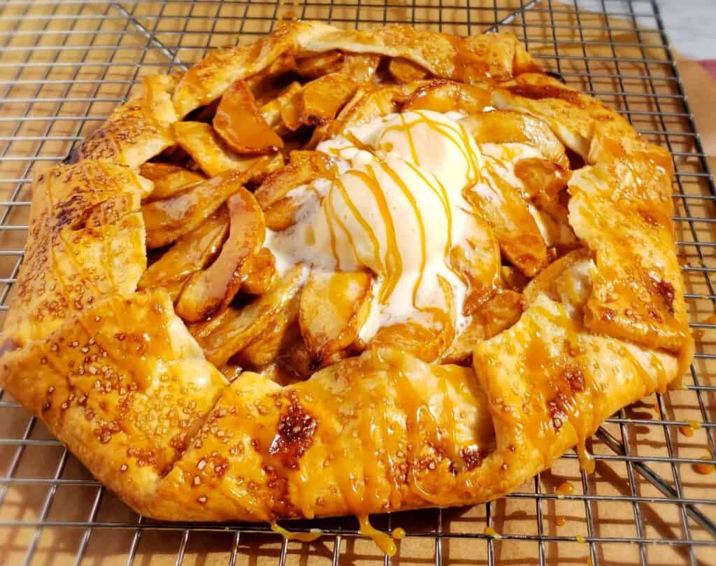 Apple galette with caramel drizzled on the melting ice cream. The shortcut apple pie is placed on a wire rack