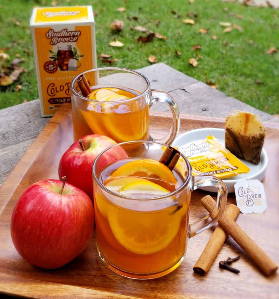 Sweet tea apple cider mugs on a wooden plate outside on a table with fallen leaves. Southern Breeze Sweet Tea bags on the table.