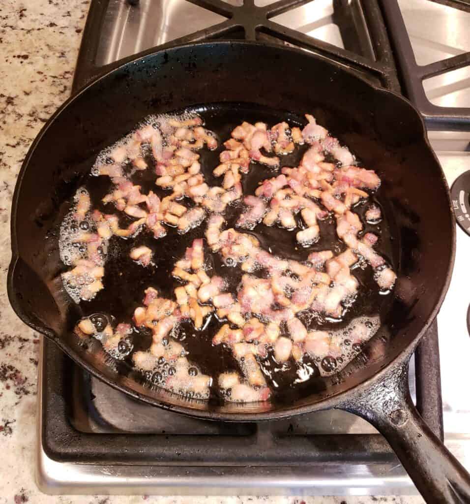 Chopped bacon frying in a cast iron skillet