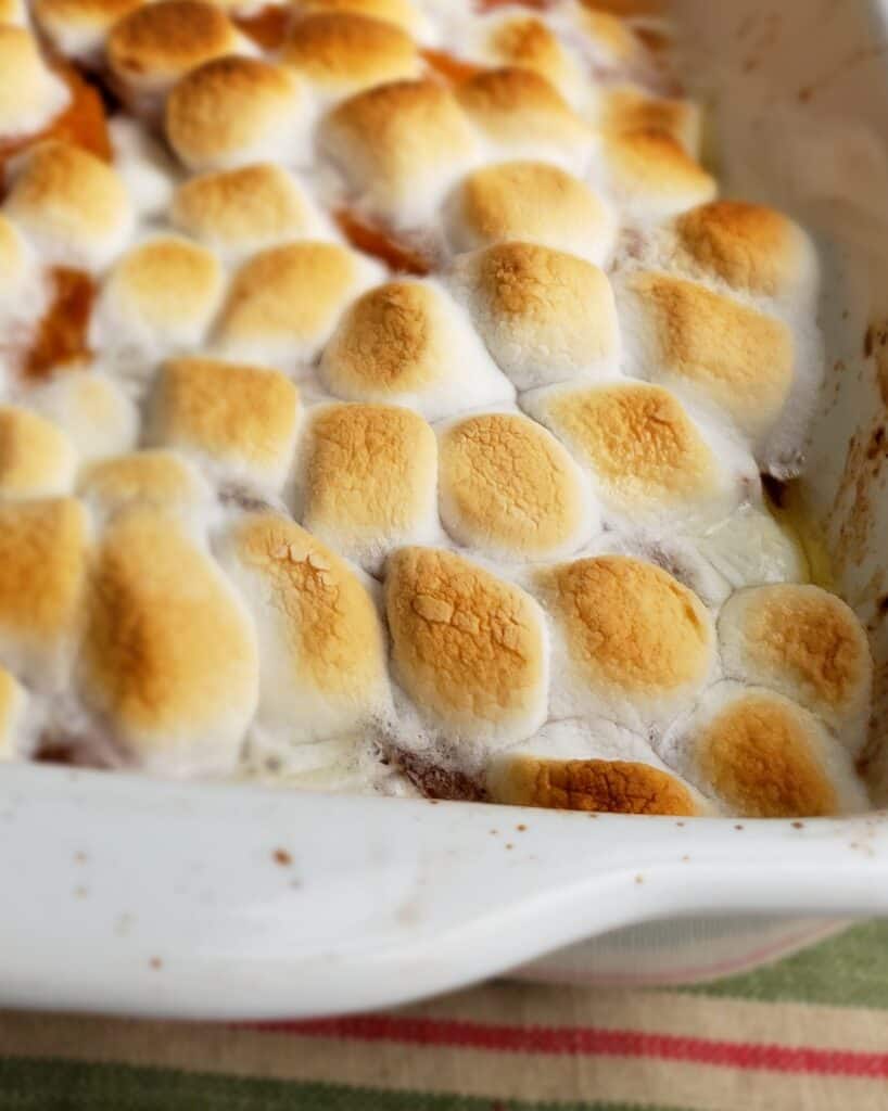 Toasted mini marshmallows covers candied sweet potatoes in a white casserole dish