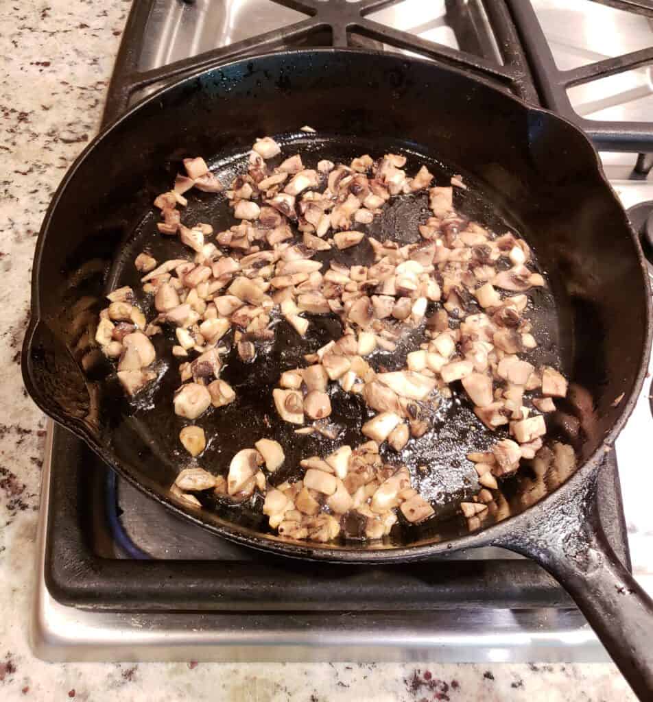 Chopped mushrooms cooking bacon drippings in a cast iron skillet