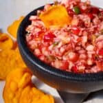 Cranberry Apple Jalapeno Salsa in a black salsa dish with sweet potato chips in it and around the dish