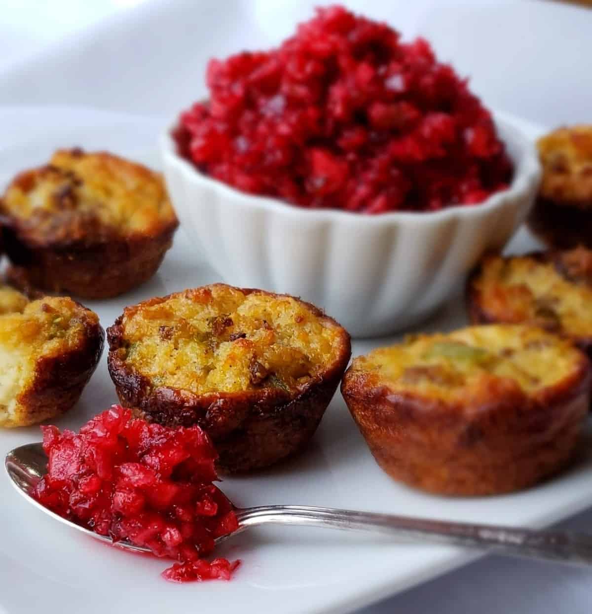 Cranberry salsa on a spoon next to a bowl of salsa surrounded by mini cups of cornbread dressing