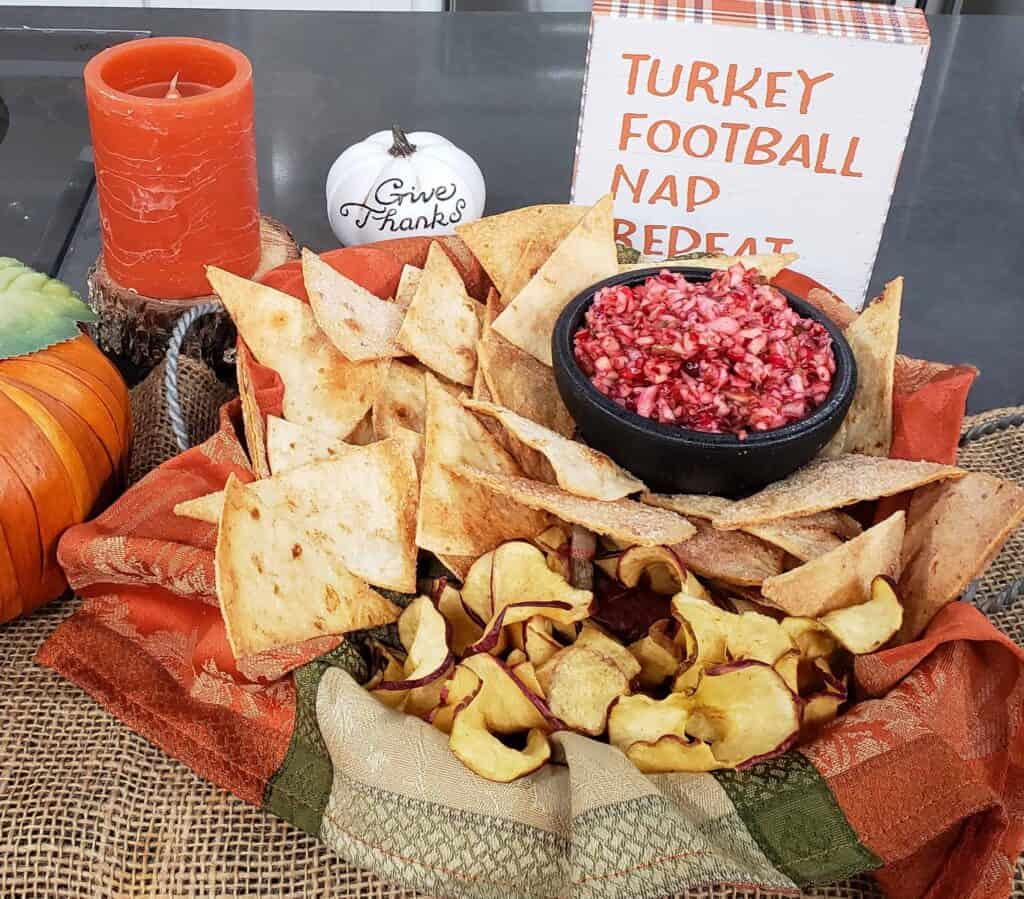 Cranberry Apple Jalapeno Salsa in a black salsa dish with with homemade cinnamon sugar tortilla chips in a decorative fall napkin and a sign that says Turkey, Football, Nap, Repeat