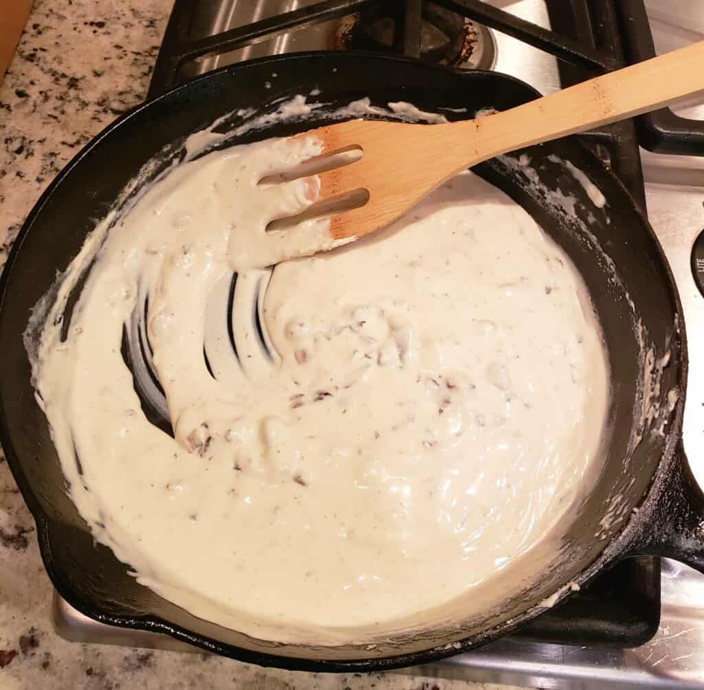 Cream cheese melting in chopped mushrooms in a cast iron skillet