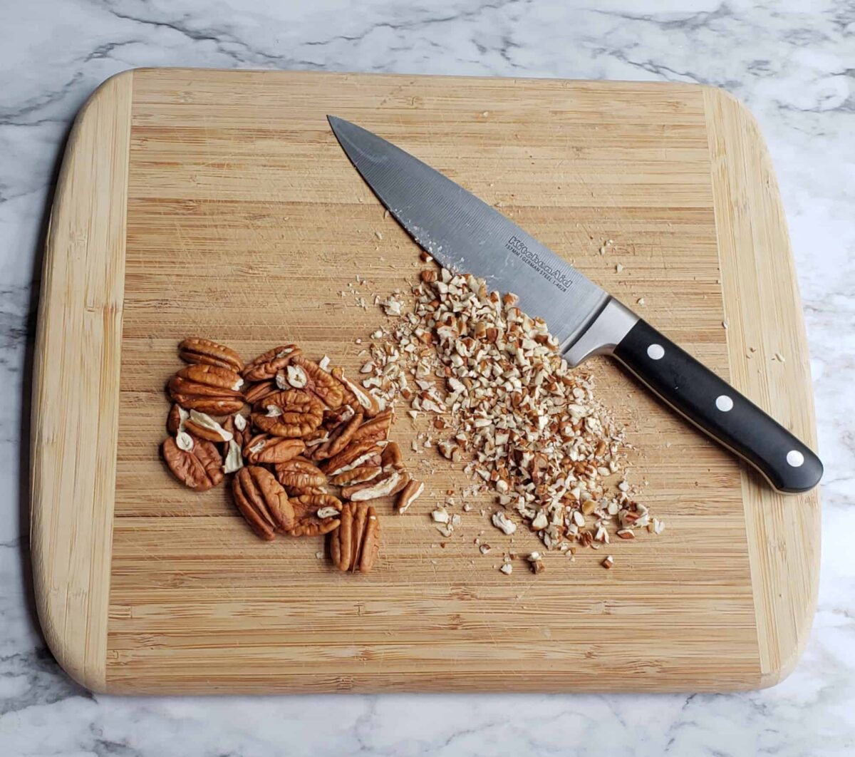 Whole pecans and finely chopped pecans on a wooden cutting board with a chefs knife