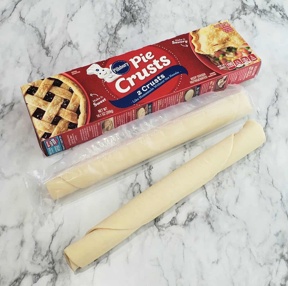 Pillsbury refrigerated pie dough rolled up with box beside 2 rolls