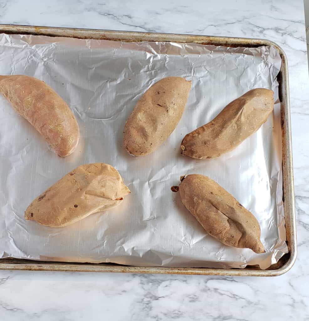 5 baked sweet potatoes on a foil-lined baking sheet