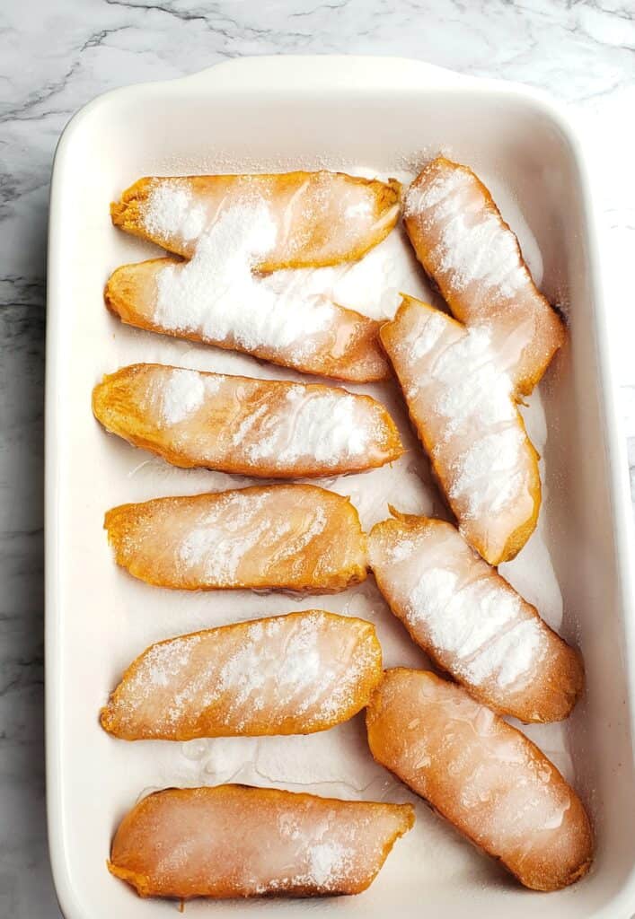 Sweet Potatoes halves are coated with sugar and drizzled with corn syrup and butter in a white casserole dish before baking