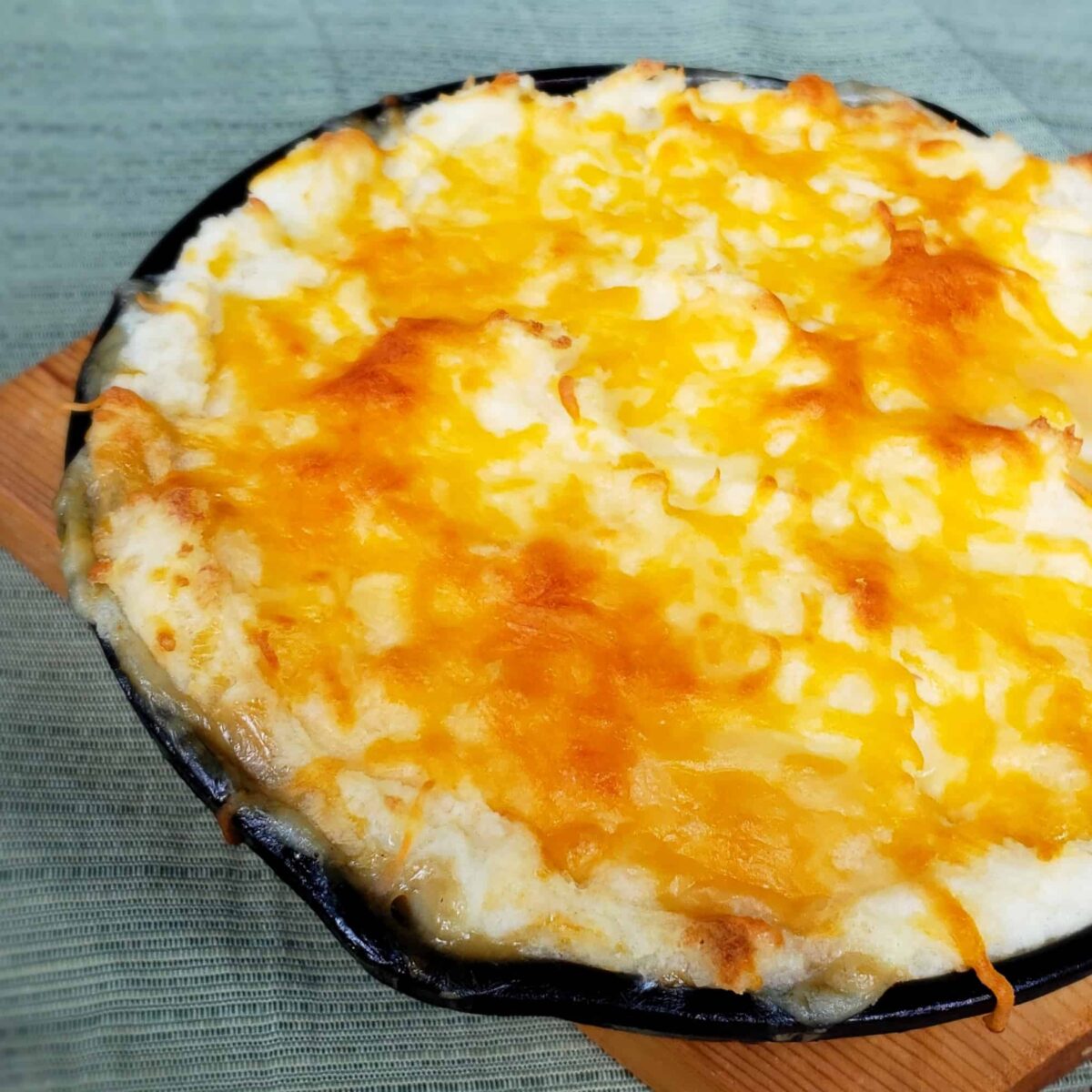Turkey Shepherds Pie baked in a cast iron skillet and place on an orange towel topped with cheese.