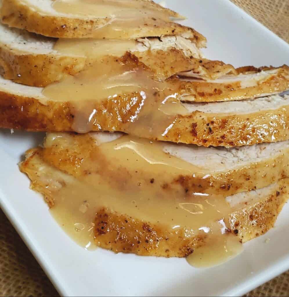 Slices of turkey breast on a white plate with gravy drizzled over the turkey