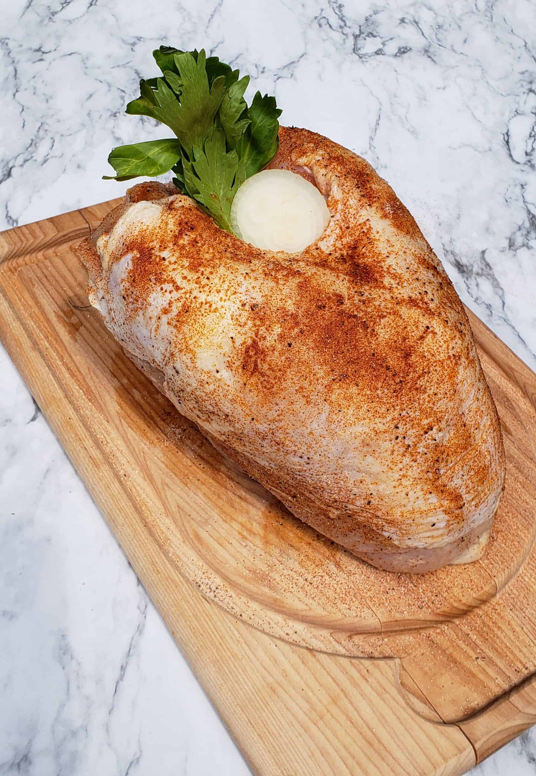 Uncooked turkey breast on a wooden cutting board stuffed with celery leaves and onion on a marble surface