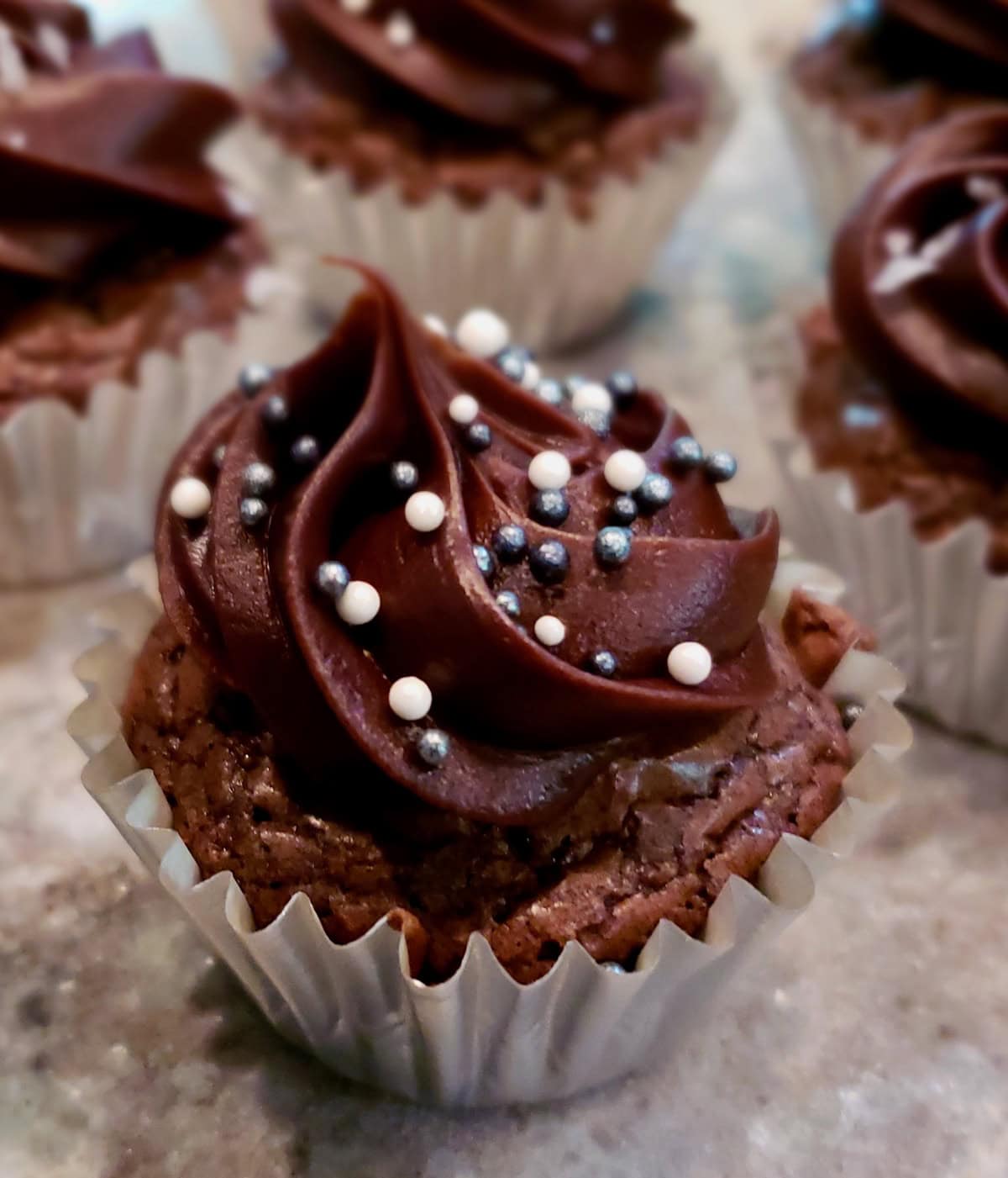 Frosted mini brownie cups in silver paper cups sprinkled with silver and white sprinkles.