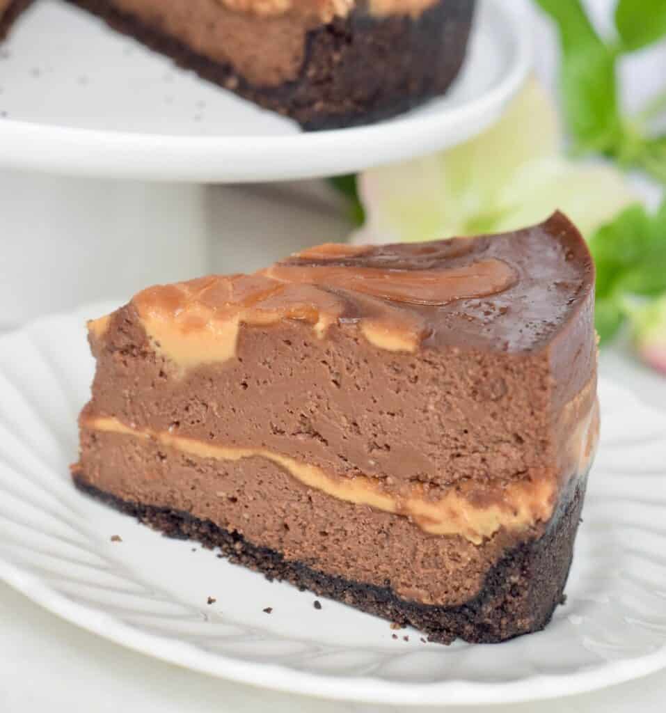 Instant Pot Chocolate Peanut Butter Swirl Cheesecake sliced and served on a white plate with a lentin rose in the background