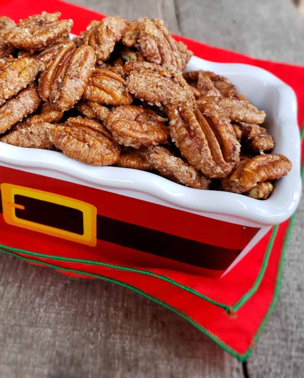 3 Ingredient Cinnamon Sugar Pecans in a Santa belt motif rectangle dish on red napkin wtih green trim