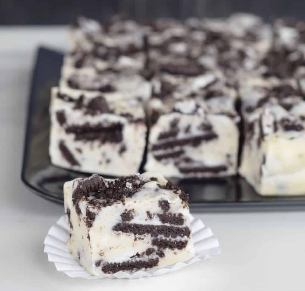 Cookies n Cream White Chocolate Fudge. No Candy thermometer needed! A black platter of fudge with one on a white candy wrapper