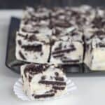 Squares of Oreo cookies and cream fudge with one on a paper liner.