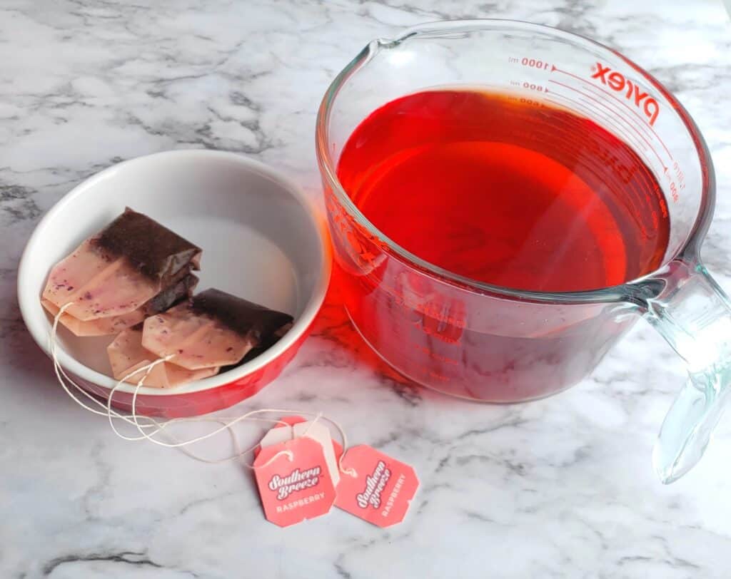 raspberry flavored Southern Breeze presweetened tea bags in red bowl next to 4 cup measuring cup.
