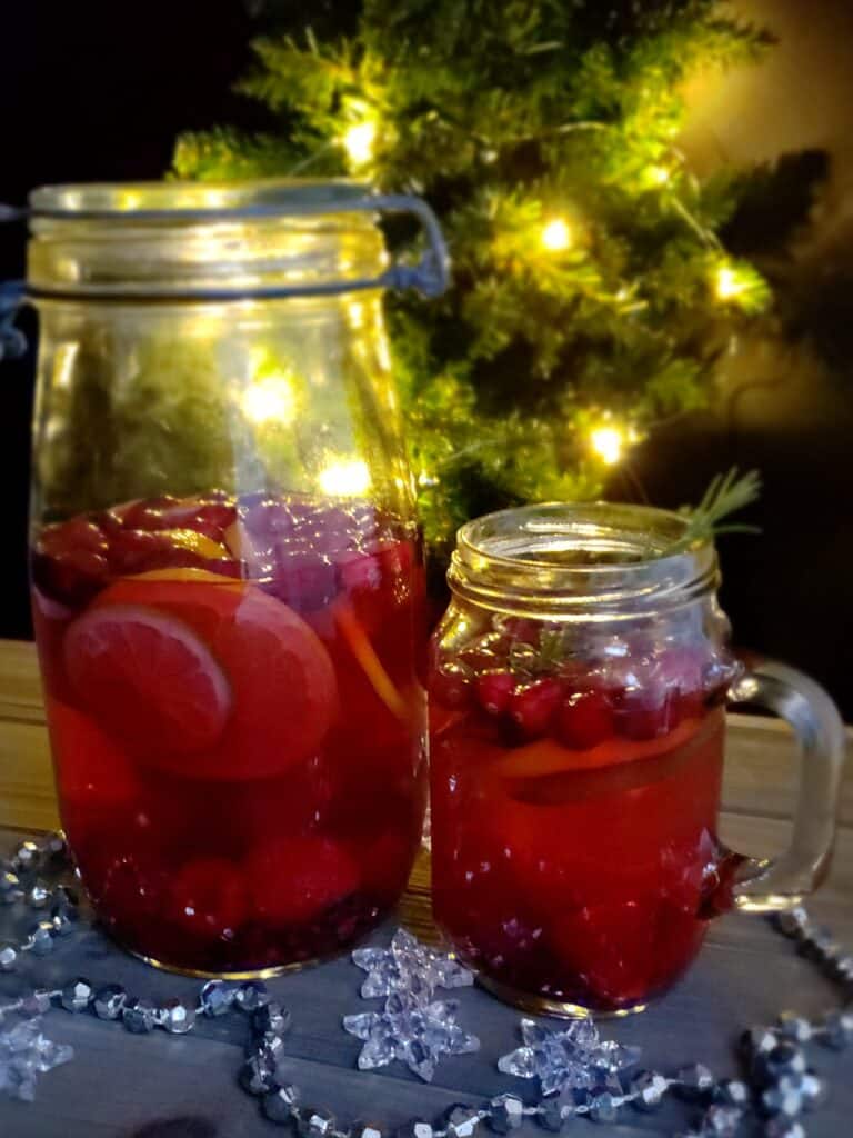 Cranberry Mocktail in jars at a Christmas tree trimming party with tree lights in background.
