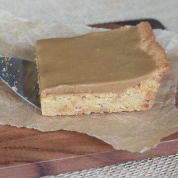 Caramel Frosted Blonde Brownie on a metal spatula on brown parchment paper.