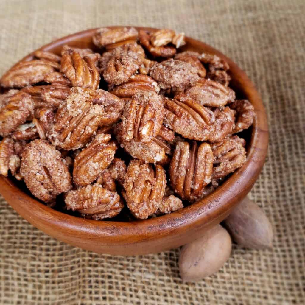 Cinnamon Sugar Pecans in a wooden bowl on burlap with 2 pecans in the shell