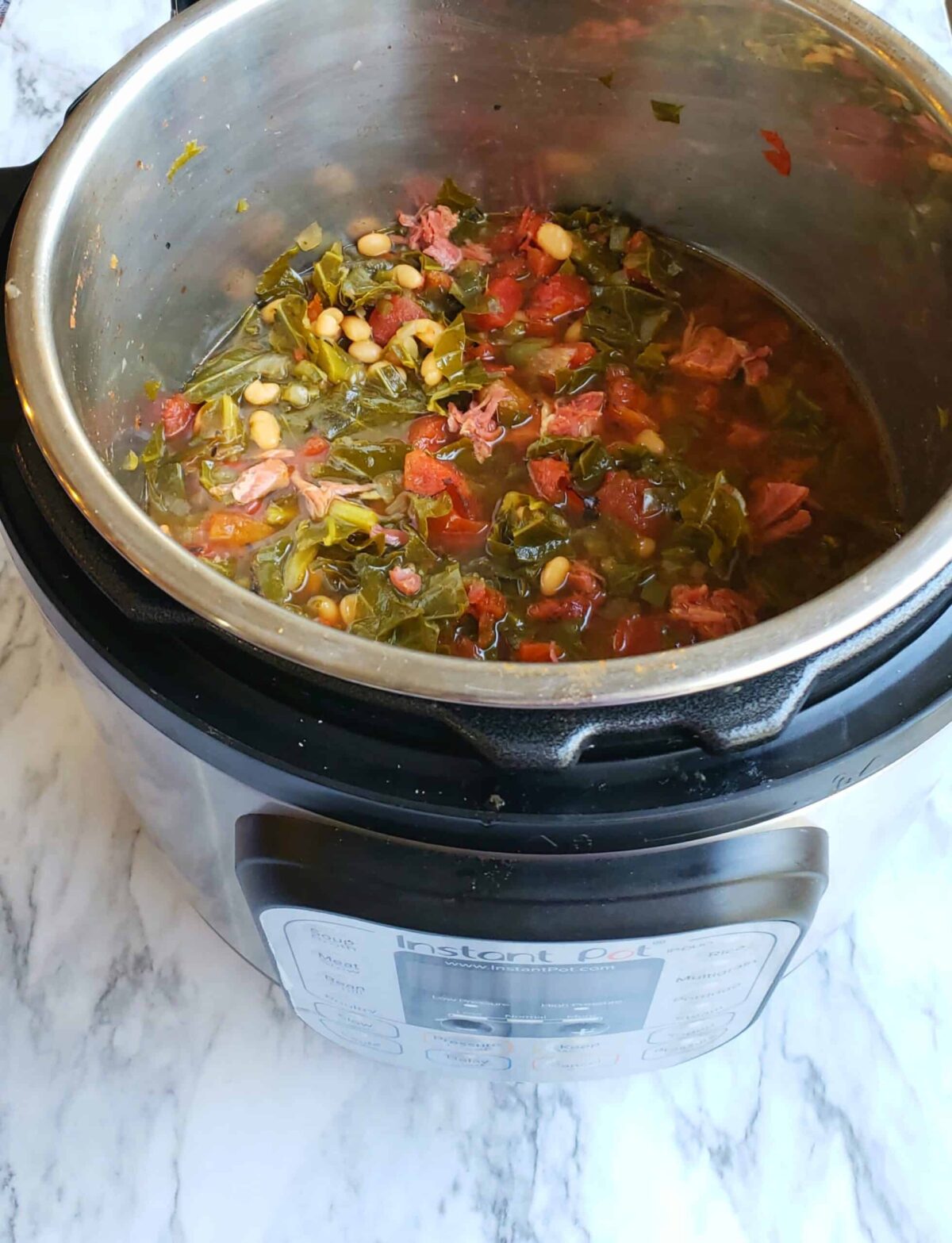 Cooked collard greens, navy beans, and tomatoes in Instant Pot with Instant Pot showing