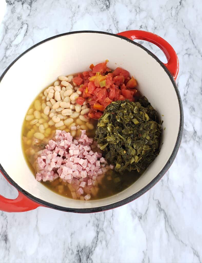 Piles of great Northern beans, turnip greens, ham, and Rotel tomatoes in a red cast iron