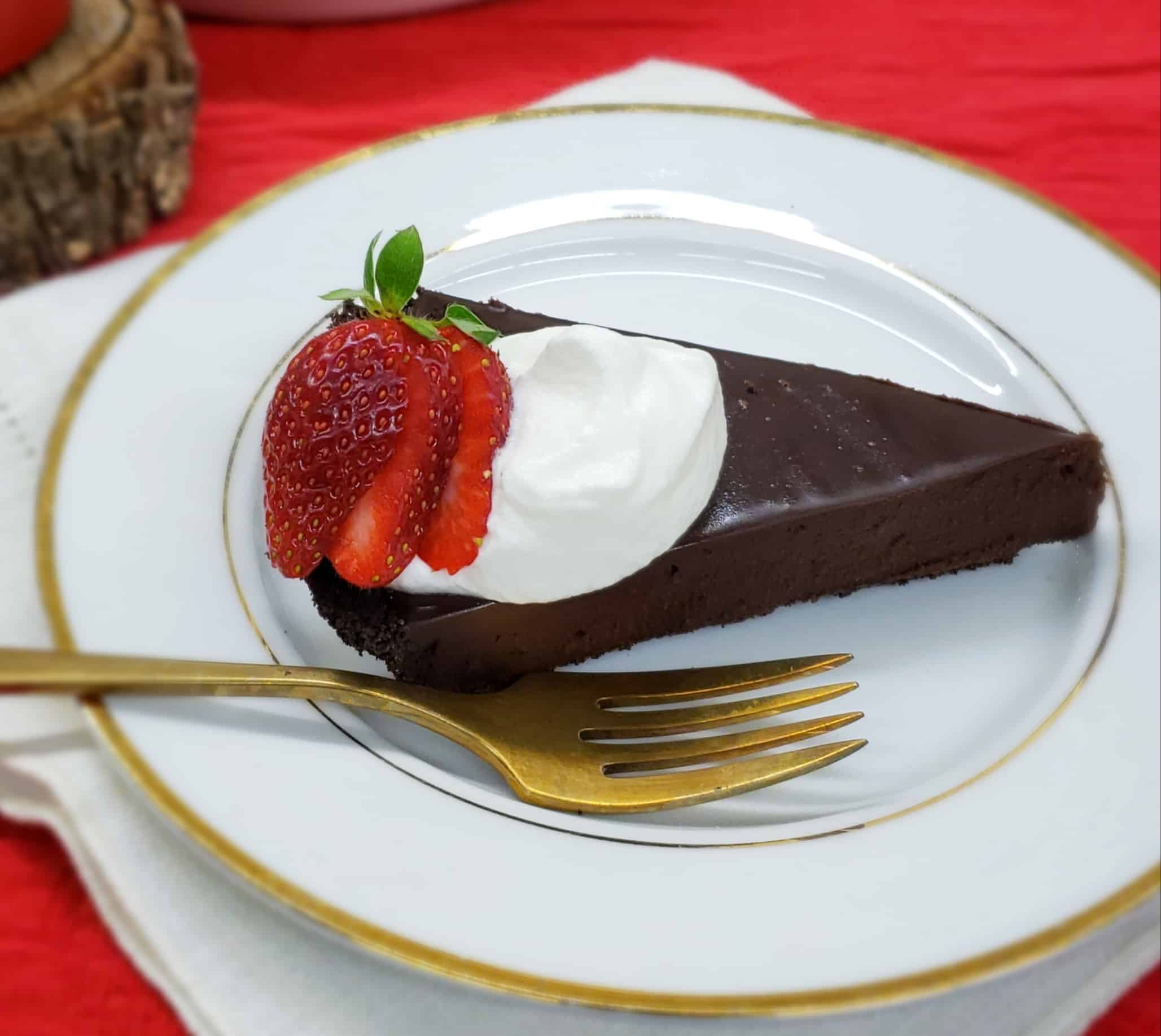 Slice of chocolate tart with whipped cream and strawberry slices on a gold rimmed plate and gold fork