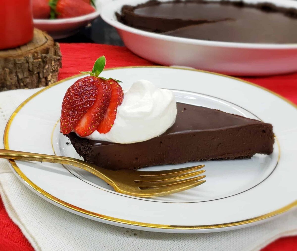 Slice of chocolate tart with whipped cream and strawberry slices on a gold rimmed plate and gold fork