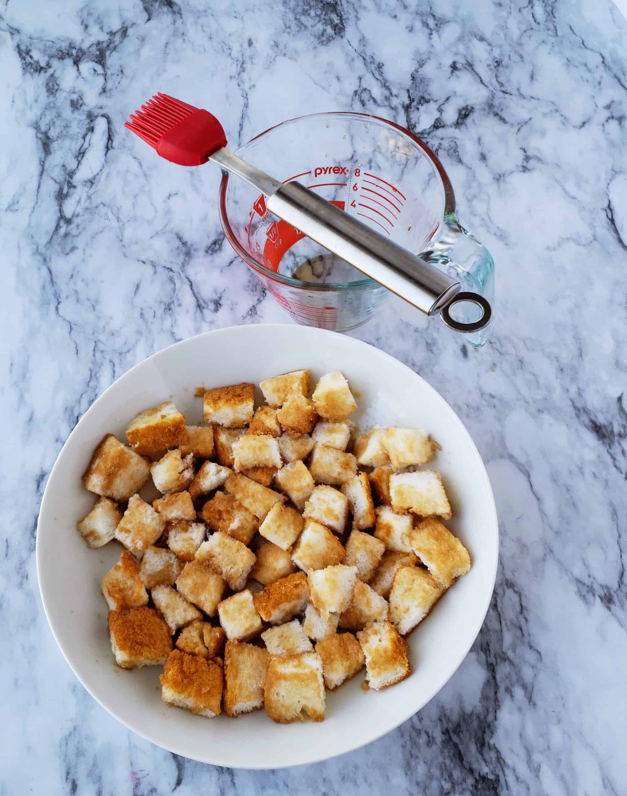 White bowl of angel food cake cubes soaked in sweet tea with pastry brush on measuring cup