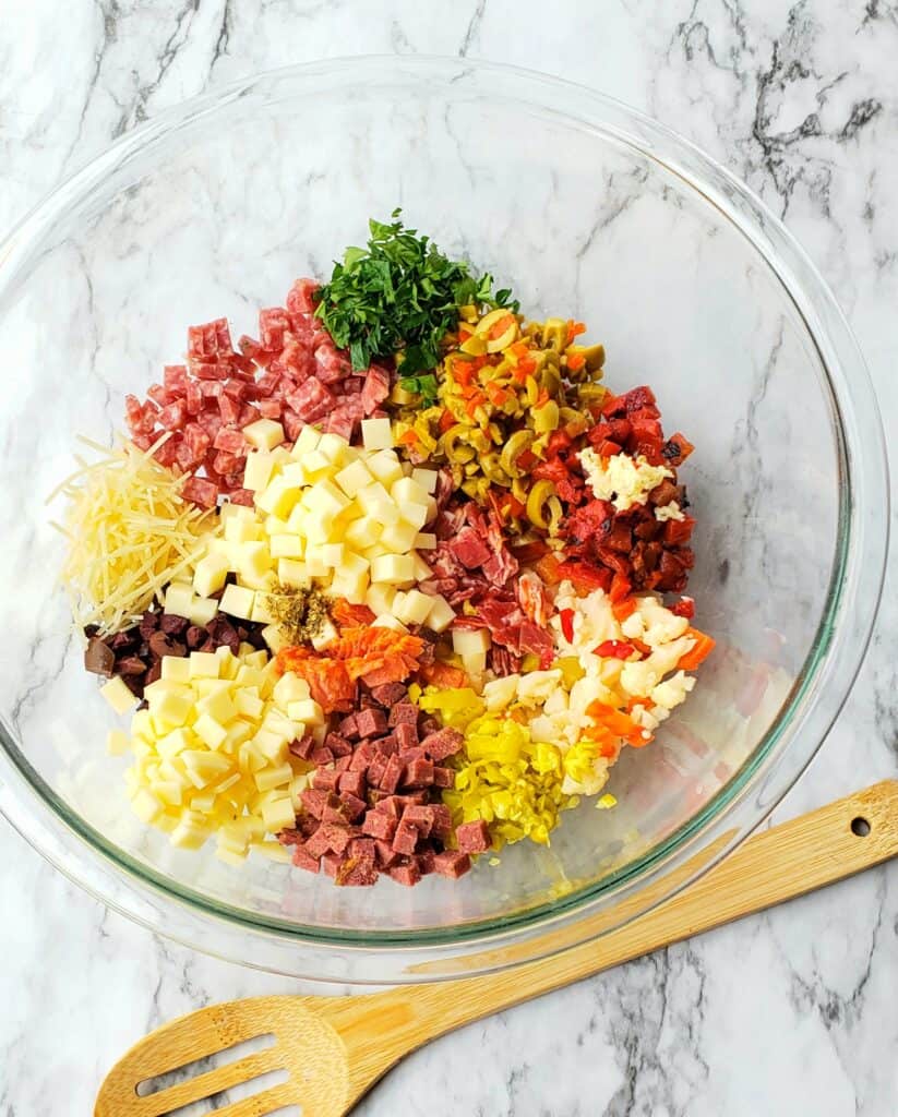 Finely chop the pickled veggies, olives, peppers. Mince the garlic and parsley. Dice the cheeses and meats.