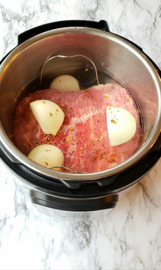 Drain and rinse the brisket and place it in a 6 quart Instant Pot with the trivet inside. The trivet helps you pull it up out of the hot liquid when its cooked. Quarter one onion and place it on top and sprinkle with the seasoning packet.
