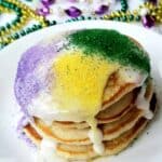 A stack of four pancakes with mardi gras beads in background.Can't make it to Mardi Gras? These shortcut banana pancakes drizzled with icing and sugar sprinkles are perfect for Fat Tuesday- also called Pancake Day!