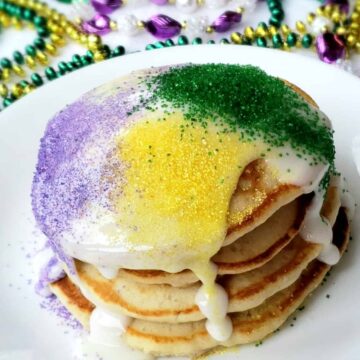 A stack of four pancakes with mardi gras beads in background.Can't make it to Mardi Gras? These shortcut banana pancakes drizzled with icing and sugar sprinkles are perfect for Fat Tuesday- also called Pancake Day!