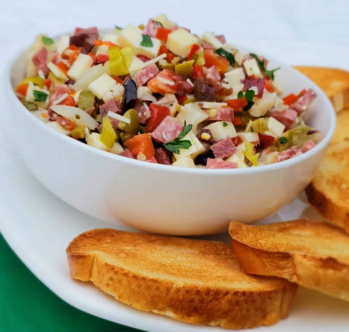 muffaletta dip in white bowl with toasted baguette slices
