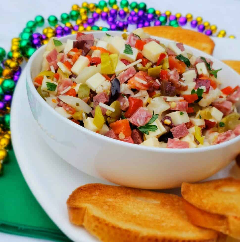 chopped meats and cheeses in a white bowl with mardi gra beads