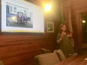 woman in low light talking with presentation board behind her