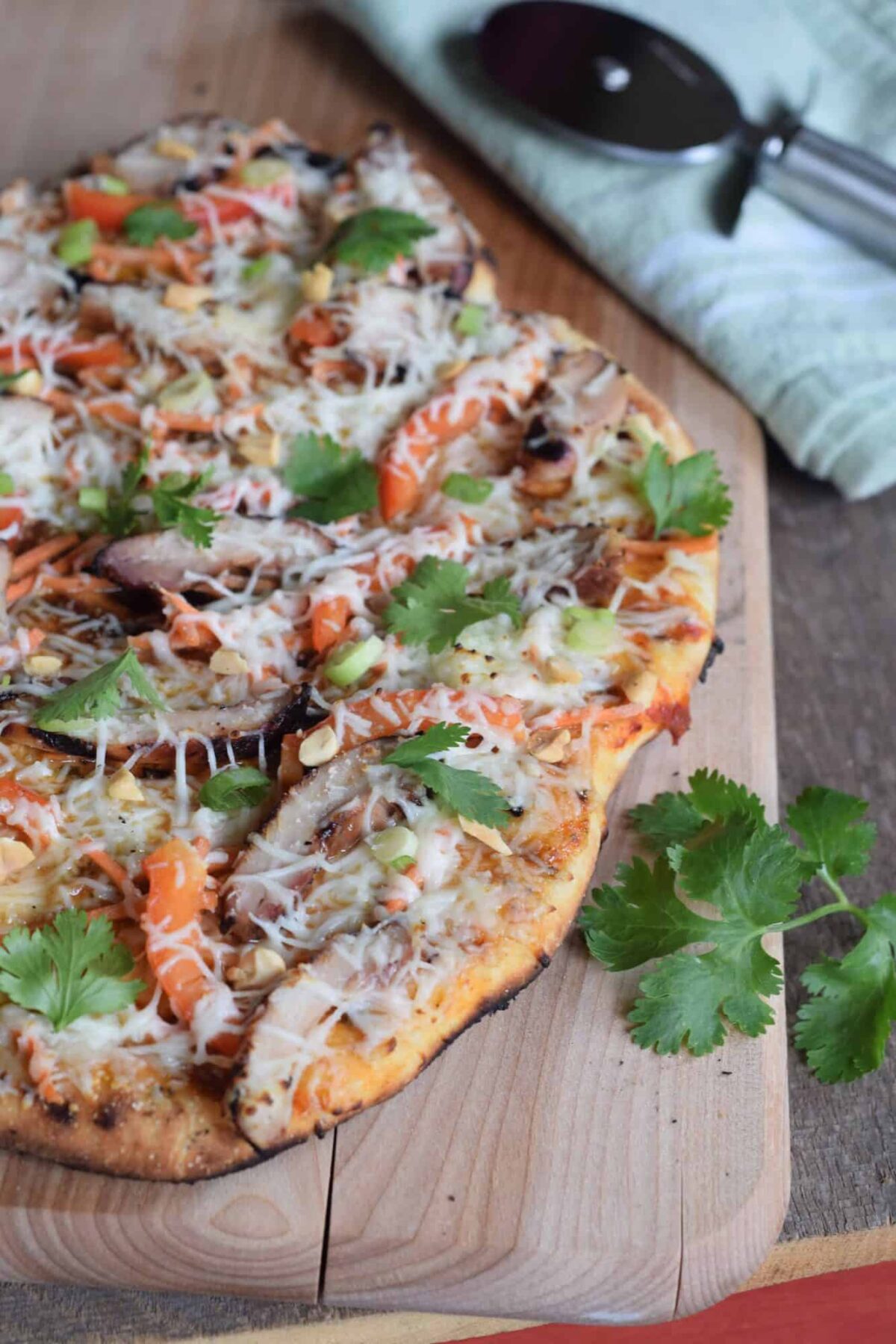 Chicken Grilled Pizza on wooden cutting board with pizza wheel on green cloth with fresh cilantro garnish