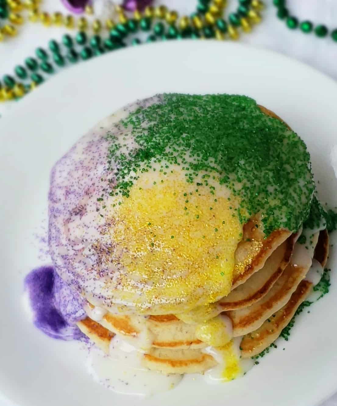 stack of 3 pancakes drizzled with icing and gold, purple and green sugar