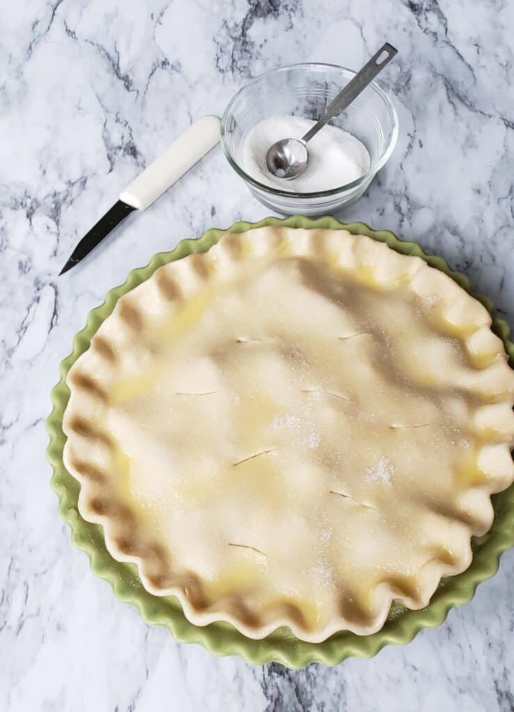 Crimped double pie crust in green pie dish with sugar on top.