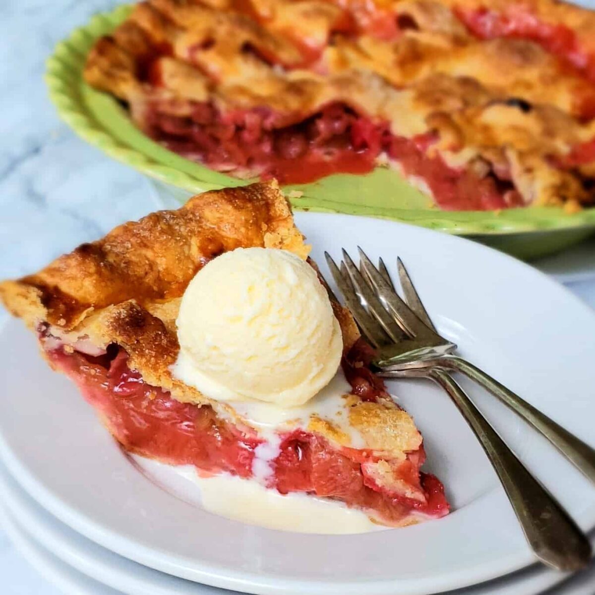  Strawberry Rhubarb Pie with scoop of vanilla ice cream on a stack of white plates and two forks.