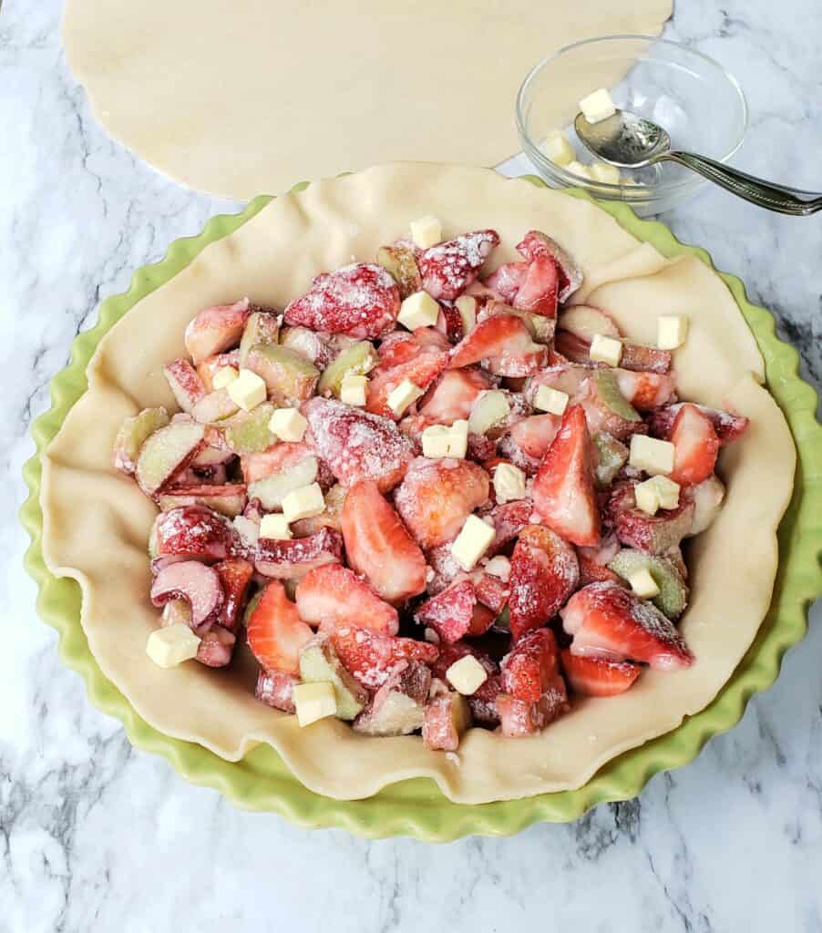 Cut up strawberries dotted with butter in pie dough in a green pie plate
