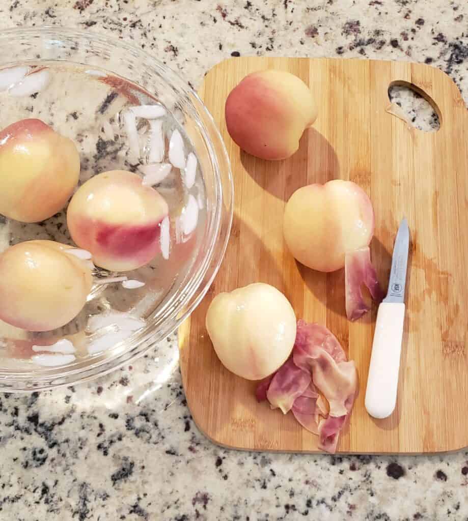 Peach skins being peeled off with white paring knife after blanching.
